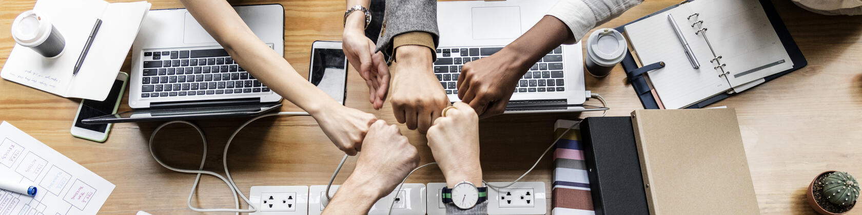 Verscheidene handen in 1 team geven elkaar een vuistje boven hun laptops