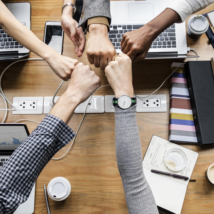 Verscheidene handen in 1 team geven elkaar een vuistje boven hun laptops